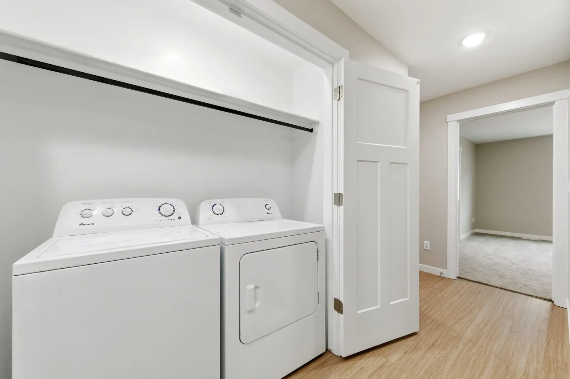 White side-by-side washer and dryer in a laundry closet with rod and shelf