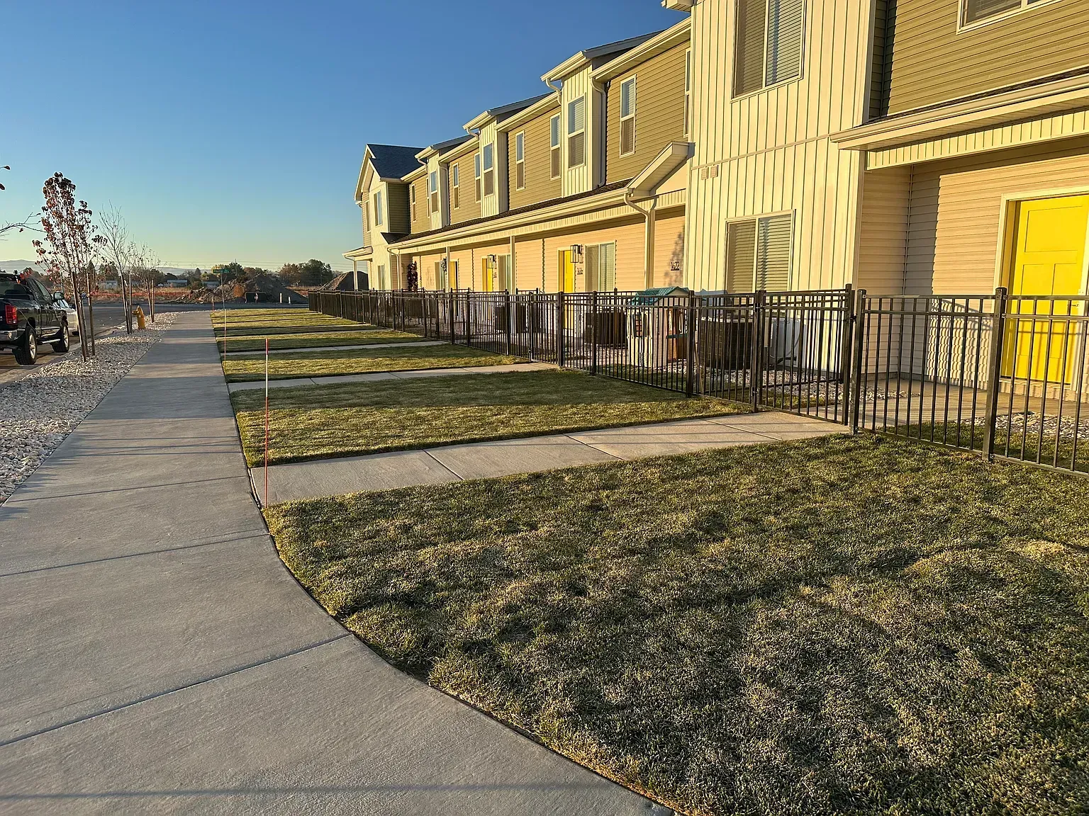 Row of townhouse-style apartments with yellow doors along a fenced walkway.
