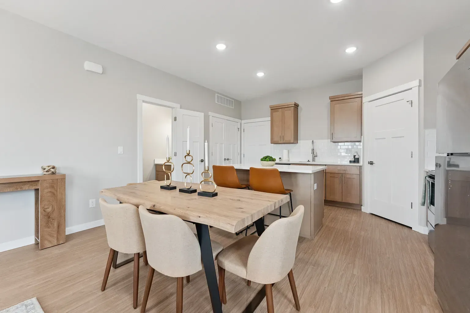 Open-plan kitchen and dining area in a modern apartment with an island, wooden cabinets, and beige chairs.