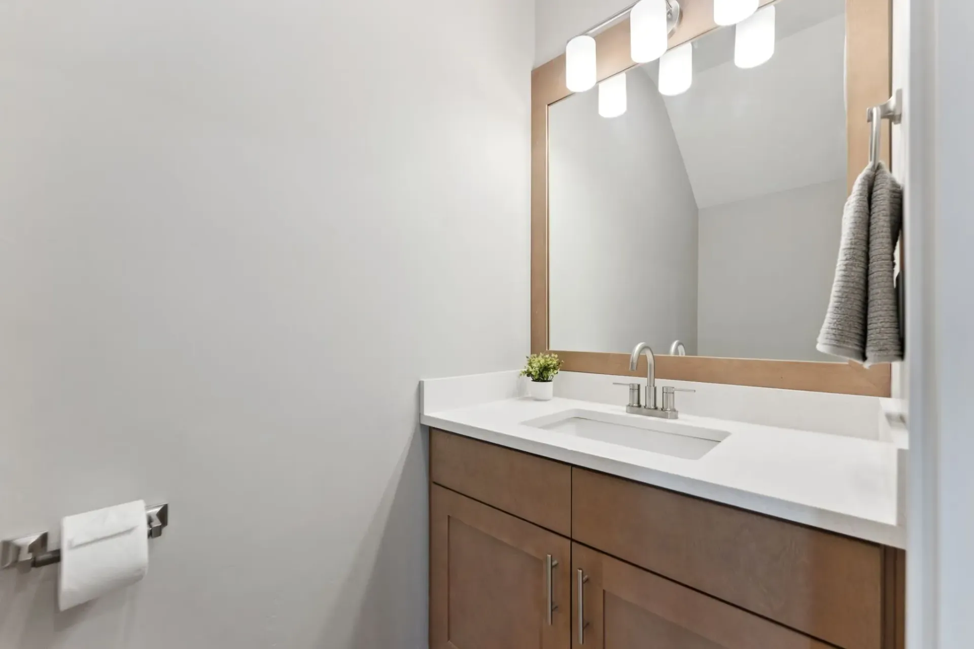 Bathroom vanity with a wood-toned cabinet, white countertop, sink, and a large framed mirror.