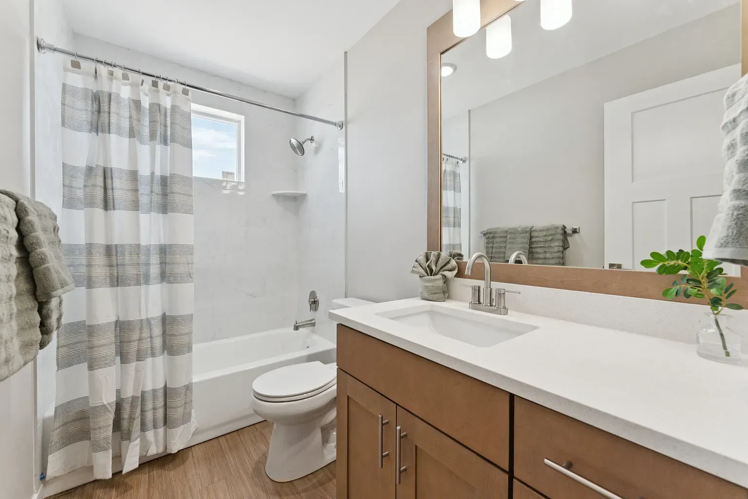 Modern apartment bathroom with vanity, mirror, shower/tub, and striped curtain.