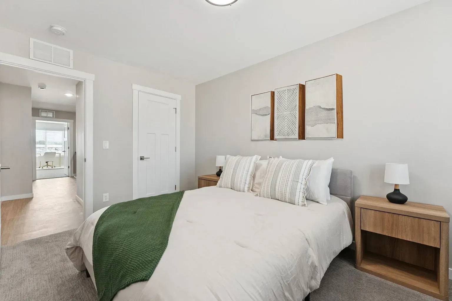 Bedroom featuring a queen bed with white bedding, pillows, two nightstands, and wall art.