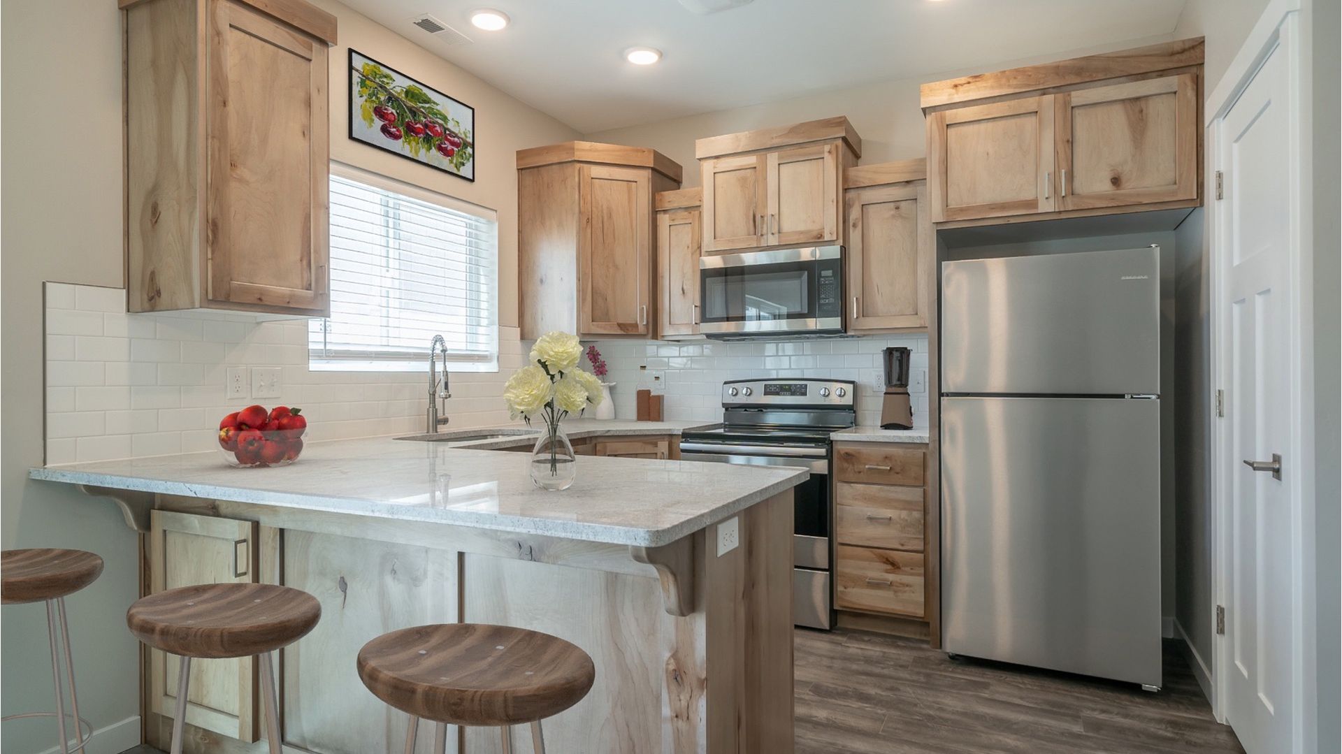 Kitchen in a modern apartment with natural wood cabinets, an island, and stainless-steel appliances.