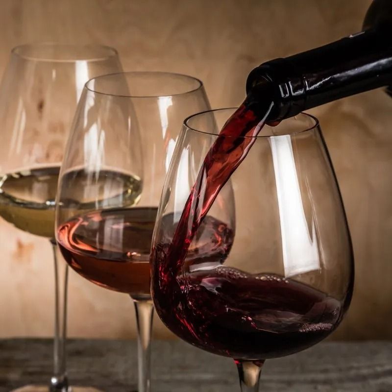 Un bicchiere di vino rosso viene versato accanto a due bicchieri di vino pieni su un tavolo.