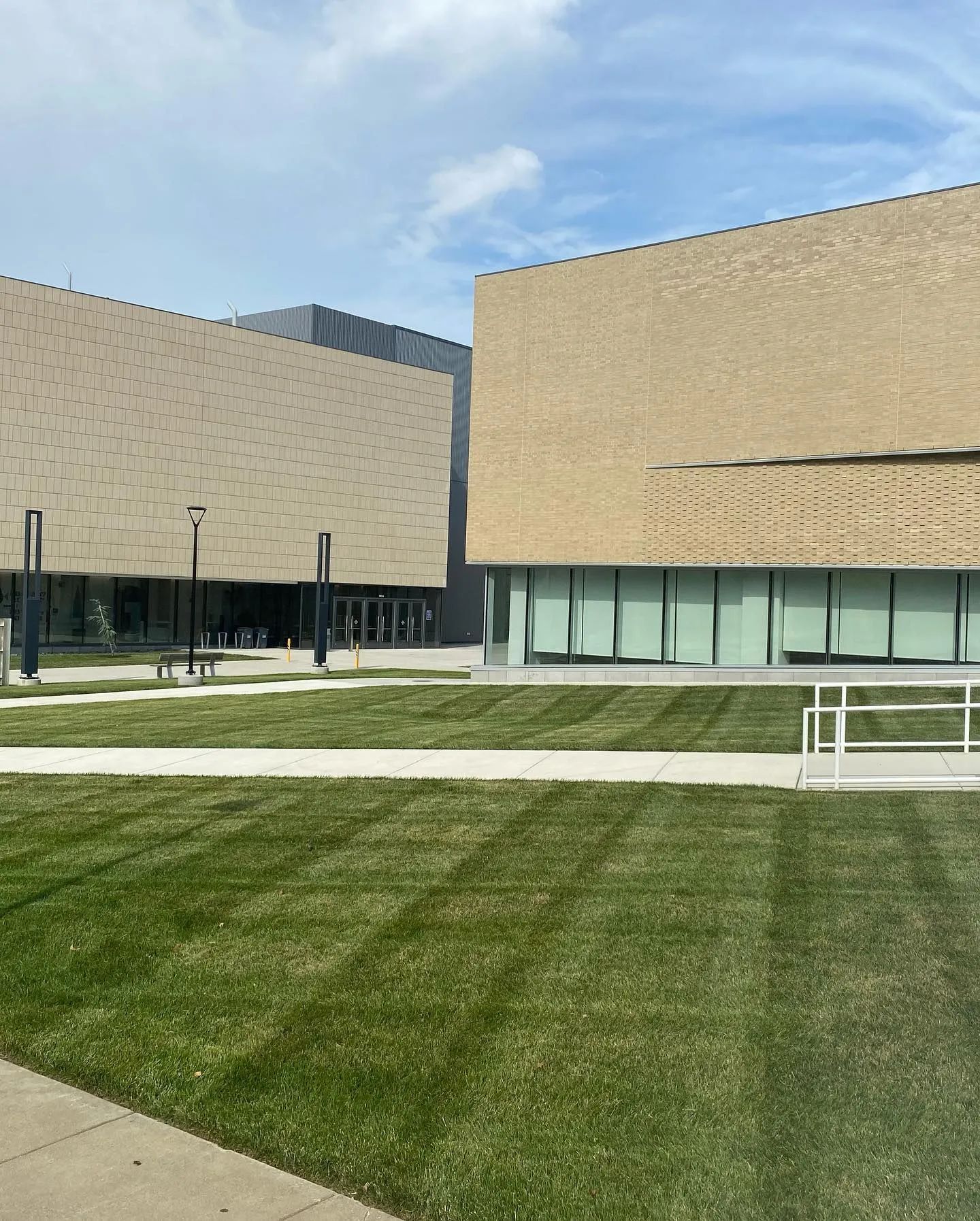 Modern campus courtyard with beige buildings, green lawn, and blue sky