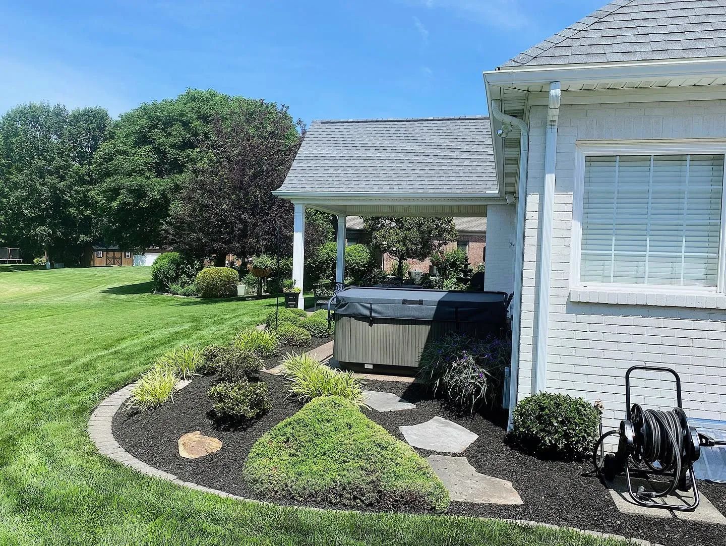 Front yard with landscaped garden, stone path, hot tub, and white house exterior under a blue sky