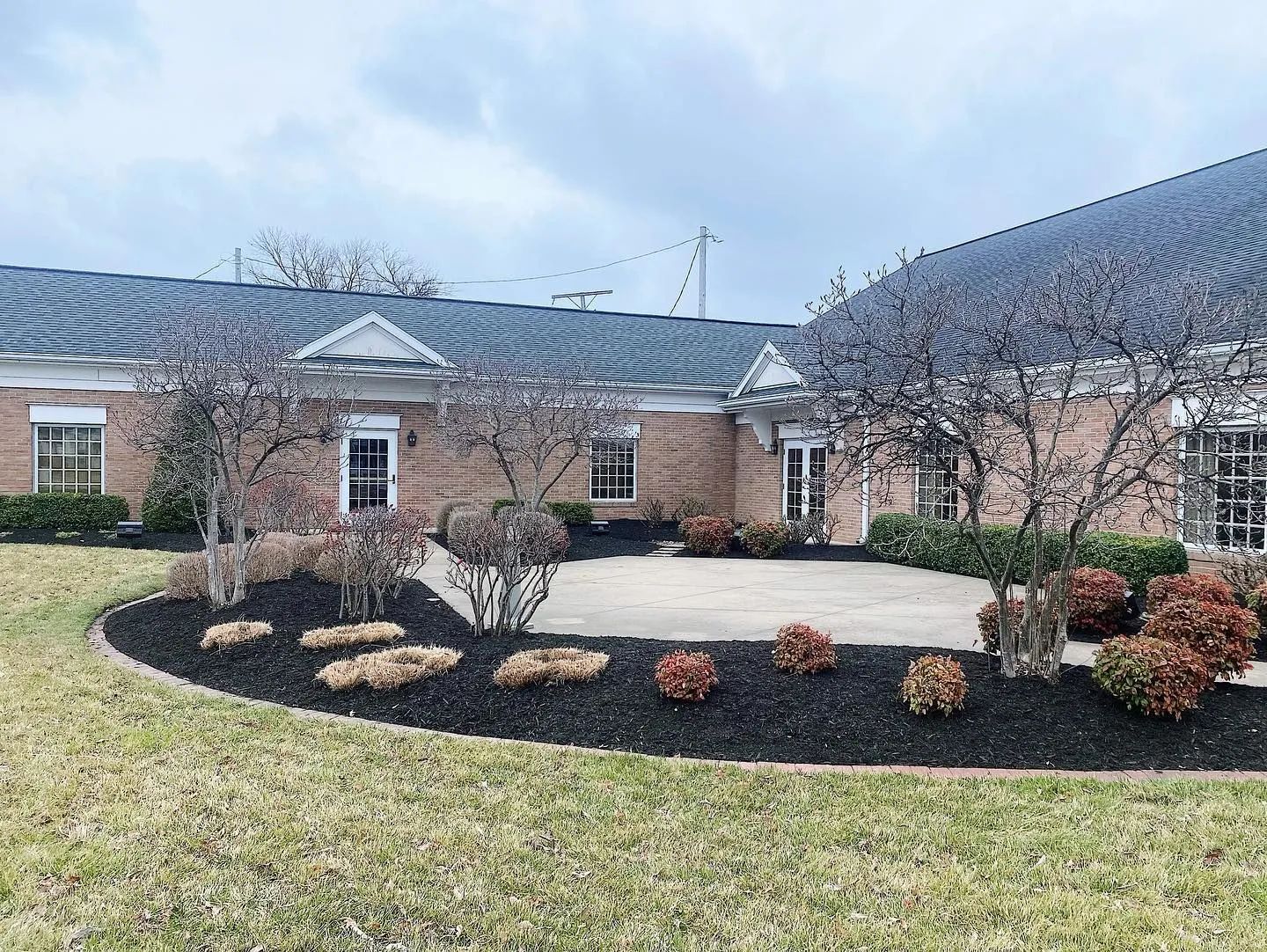 Brick house with dark roof, front walkway, and landscaped yard with shrubs and mulch.
