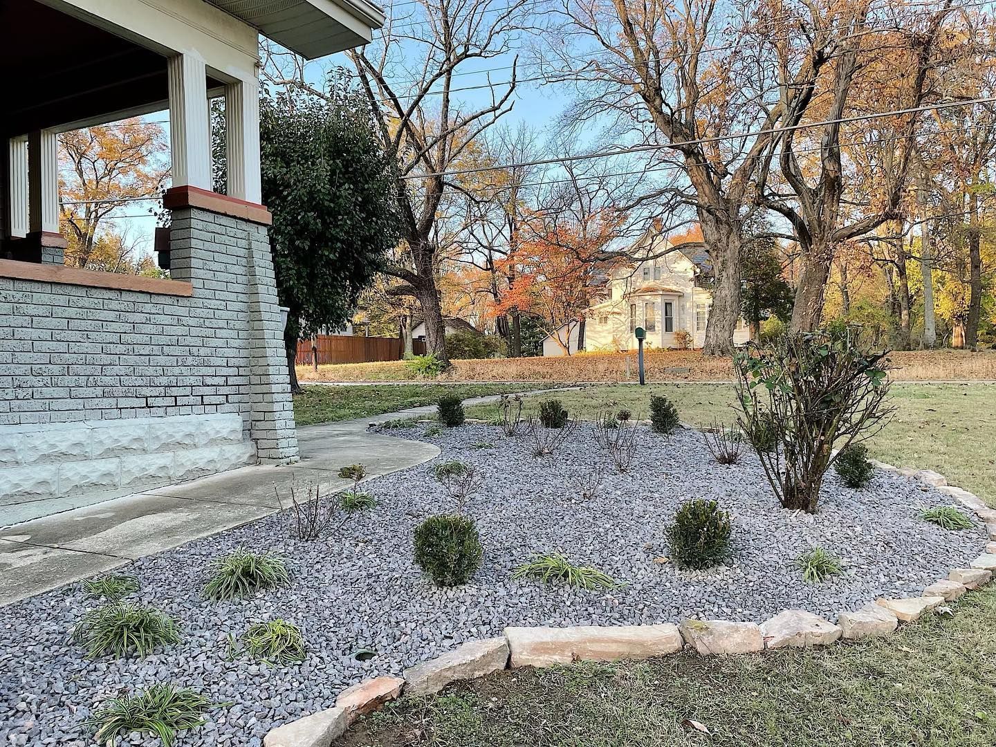 Front yard garden with purple groundcover, small shrubs, and a stone house porch in autumn