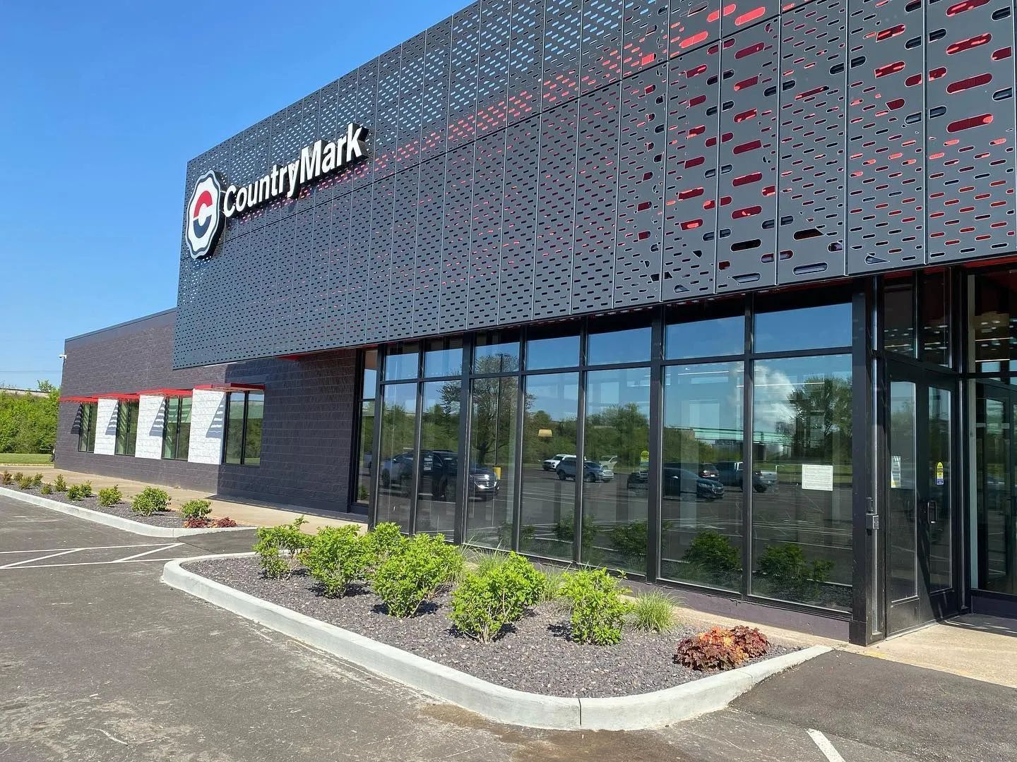 Office building exterior with glass windows, dark facade, and landscaped shrubs along the entrance.