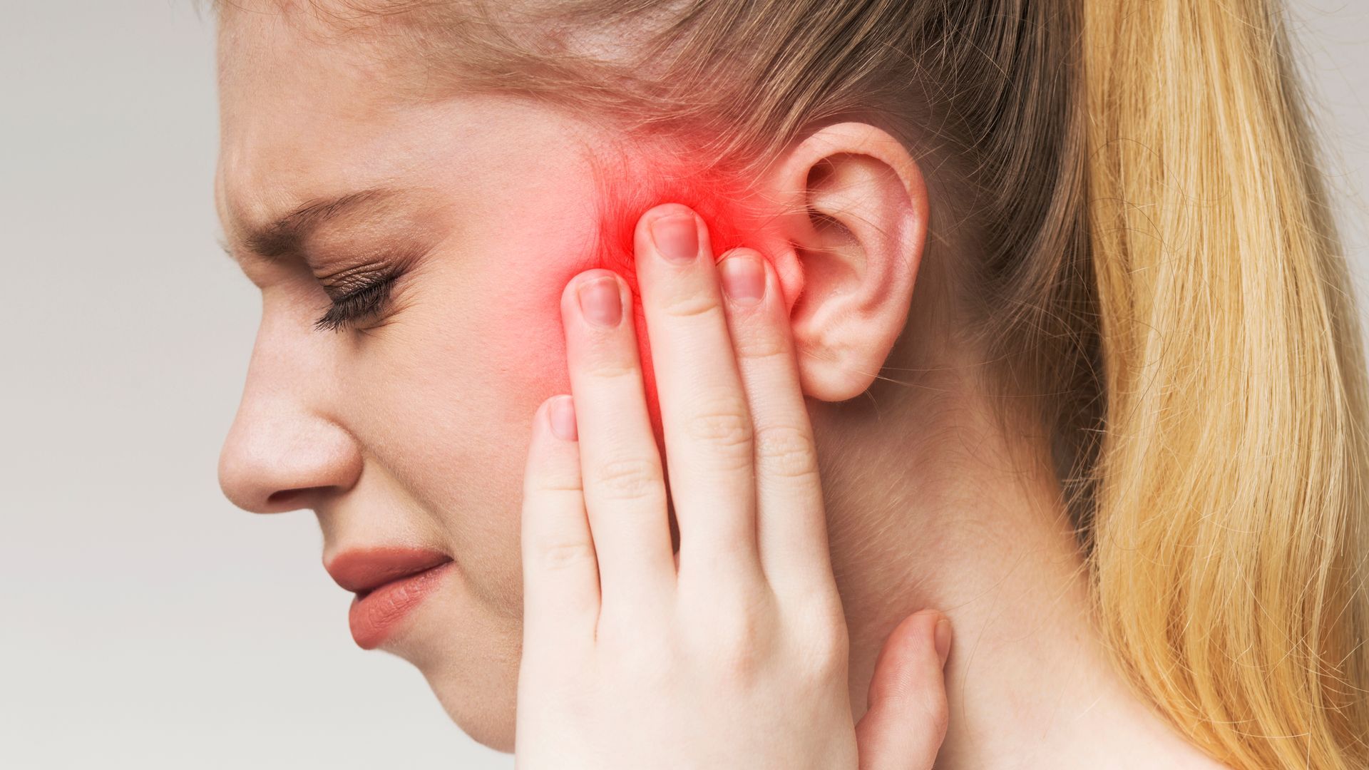 Woman holding her ear with a red glow indicating ear pain or discomfort