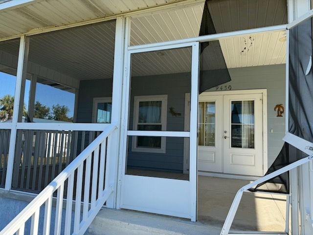 Front porch with white railings and screen door on a gray house