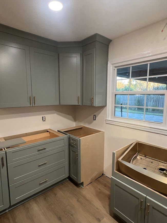 Kitchen with gray cabinets, wood floors, and a window. Cabinets are being installed.