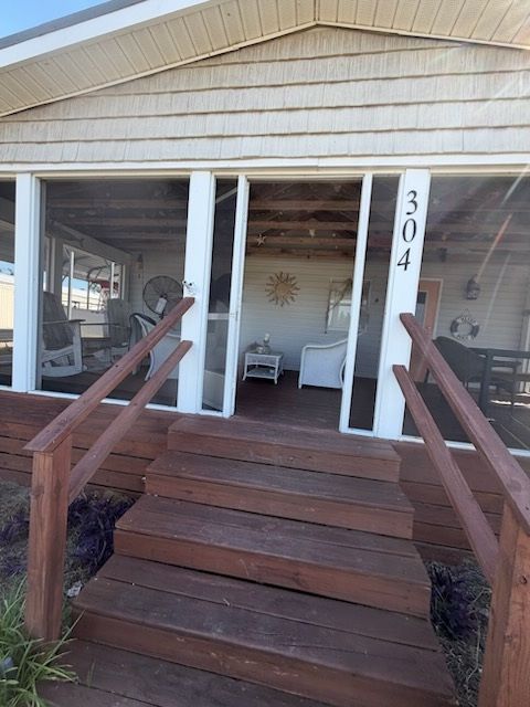 Front porch with wooden stairs and railings, white chairs, and house number 304 on the post