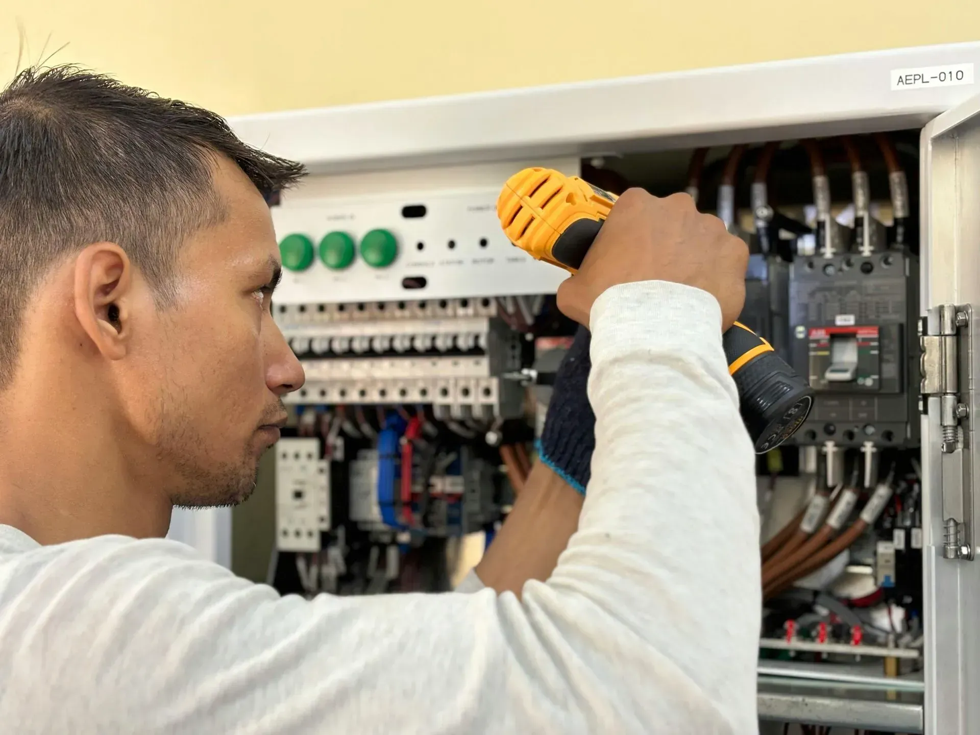 Technician using a drill to work inside an open electrical control panel