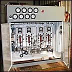 Open electrical control panel with gauges, wires, and relays mounted on a wall.
