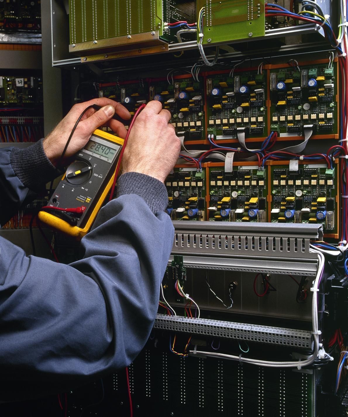 Technician testing electrical wiring inside an open equipment cabinet with a multimeter