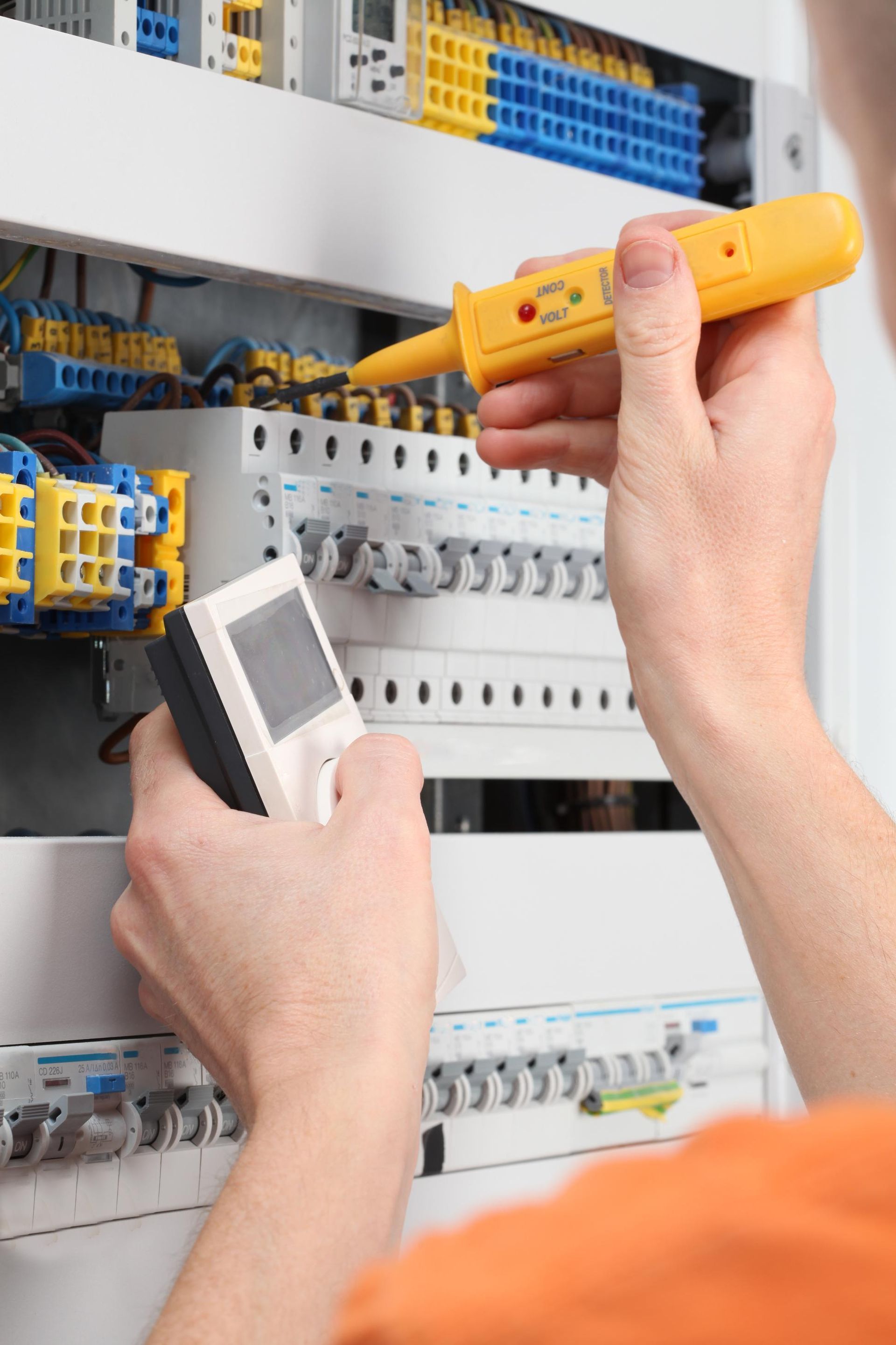 Electrician testing wiring in an open electrical panel with a voltage tester and meter.