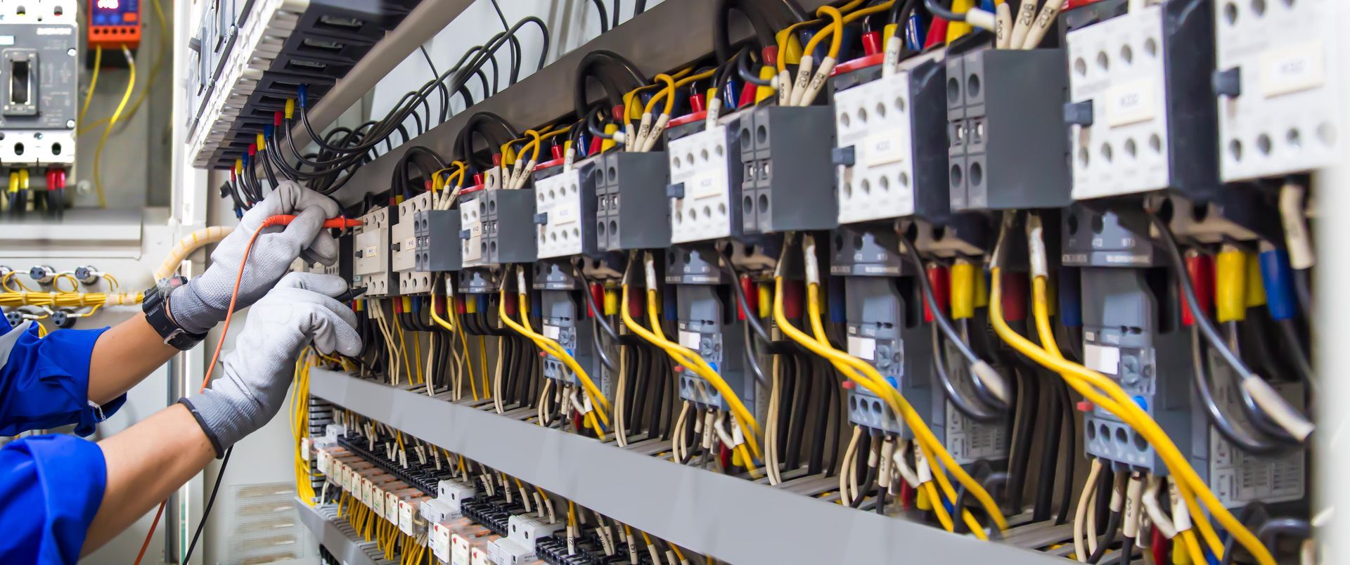 Technician wiring an electrical control panel with rows of circuit modules and cables