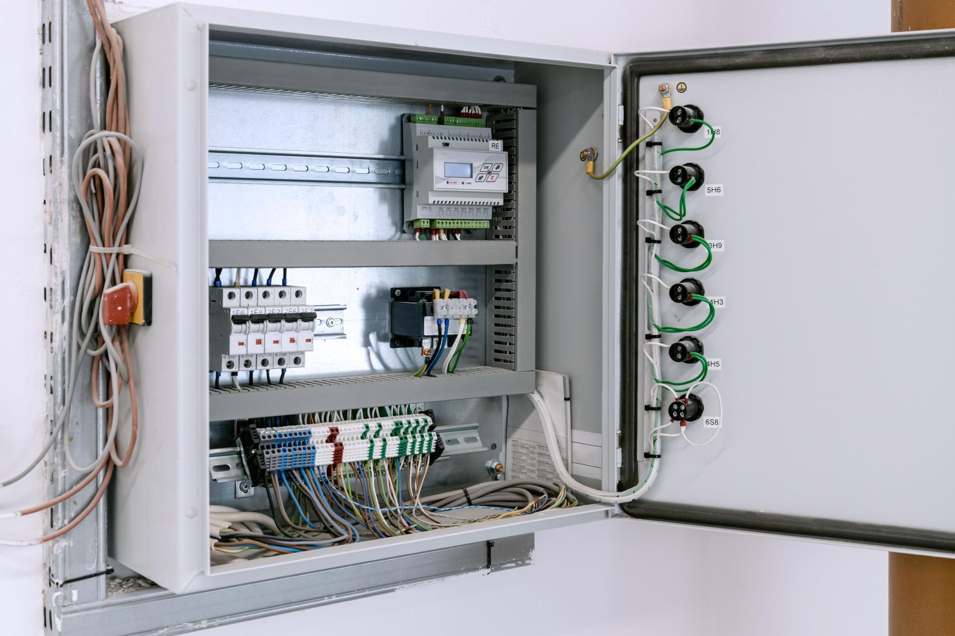 Open electrical control panel with wiring, switches, and circuit components mounted inside a wall cabinet