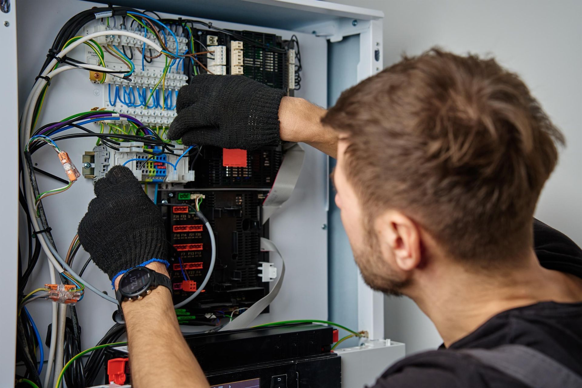 Technician wiring an open electrical control panel with gloved hands