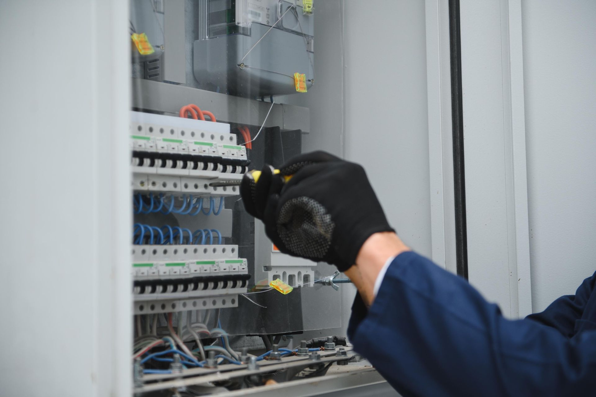 Gloved technician adjusting electrical components inside an open control panel cabinet