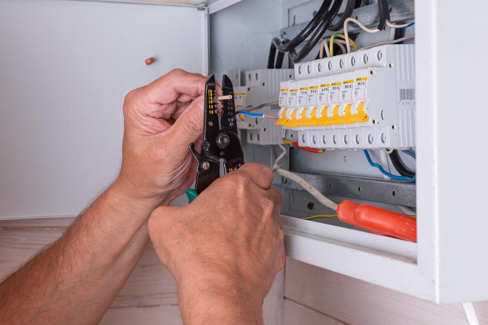 Hands wiring an electrical breaker panel inside an open cabinet.
