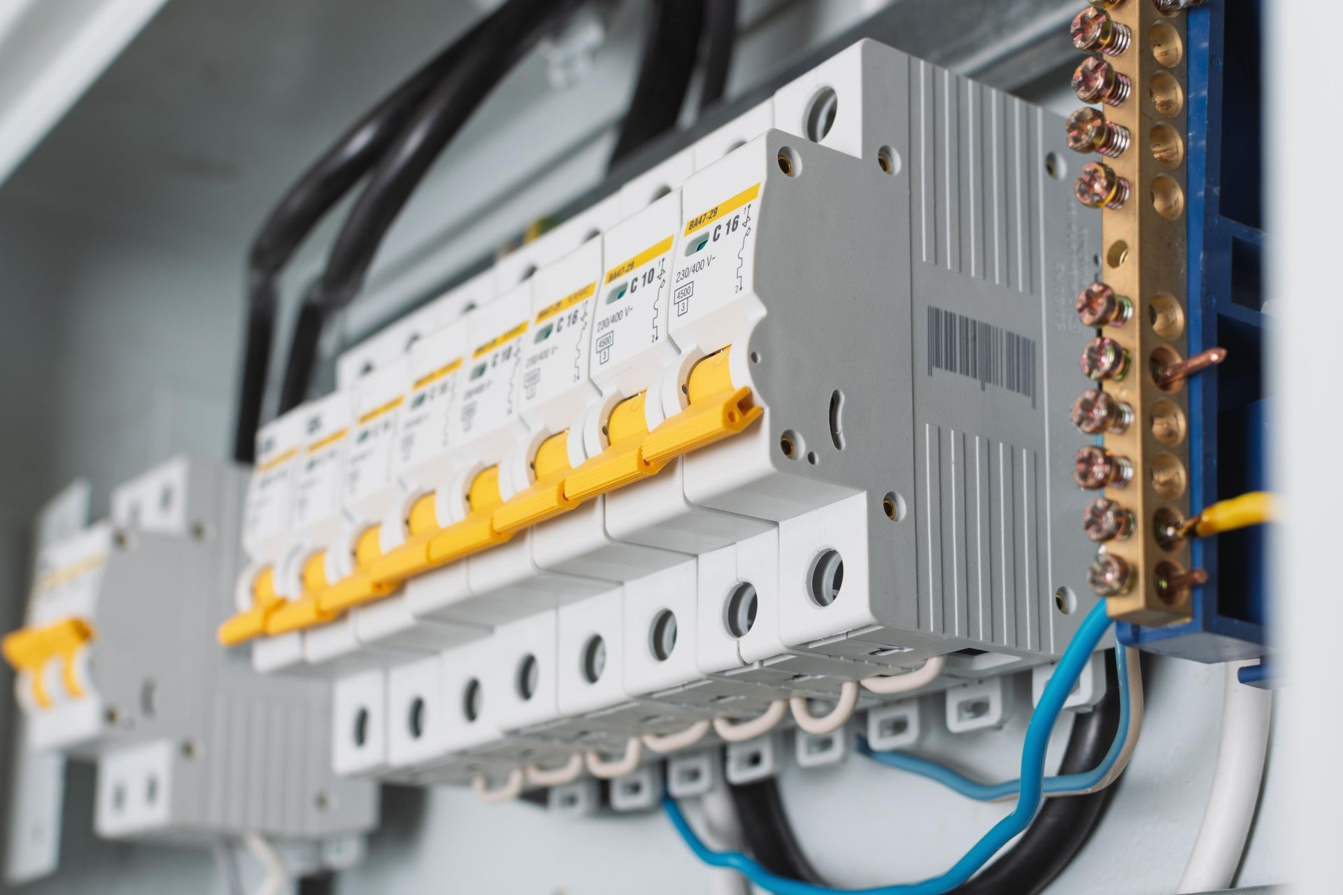Electrical circuit breaker panel with yellow switches and blue wiring in a gray control box