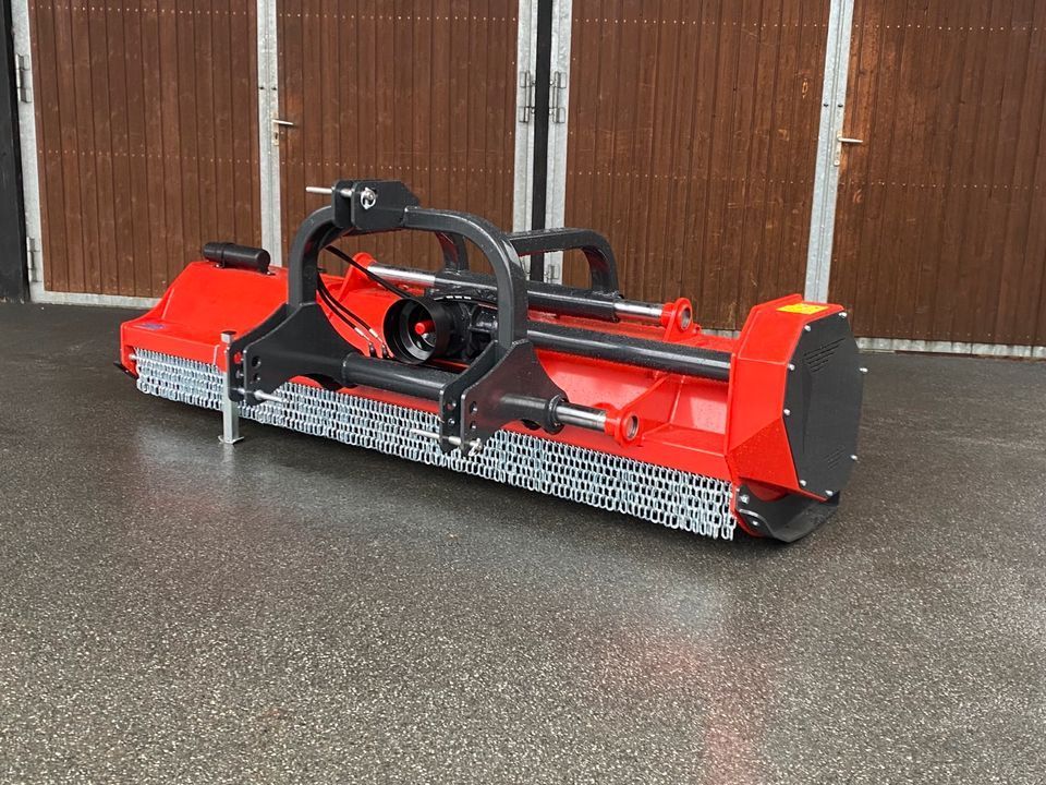 Eine rot-schwarze Maschine steht vor einer Holzgarage.