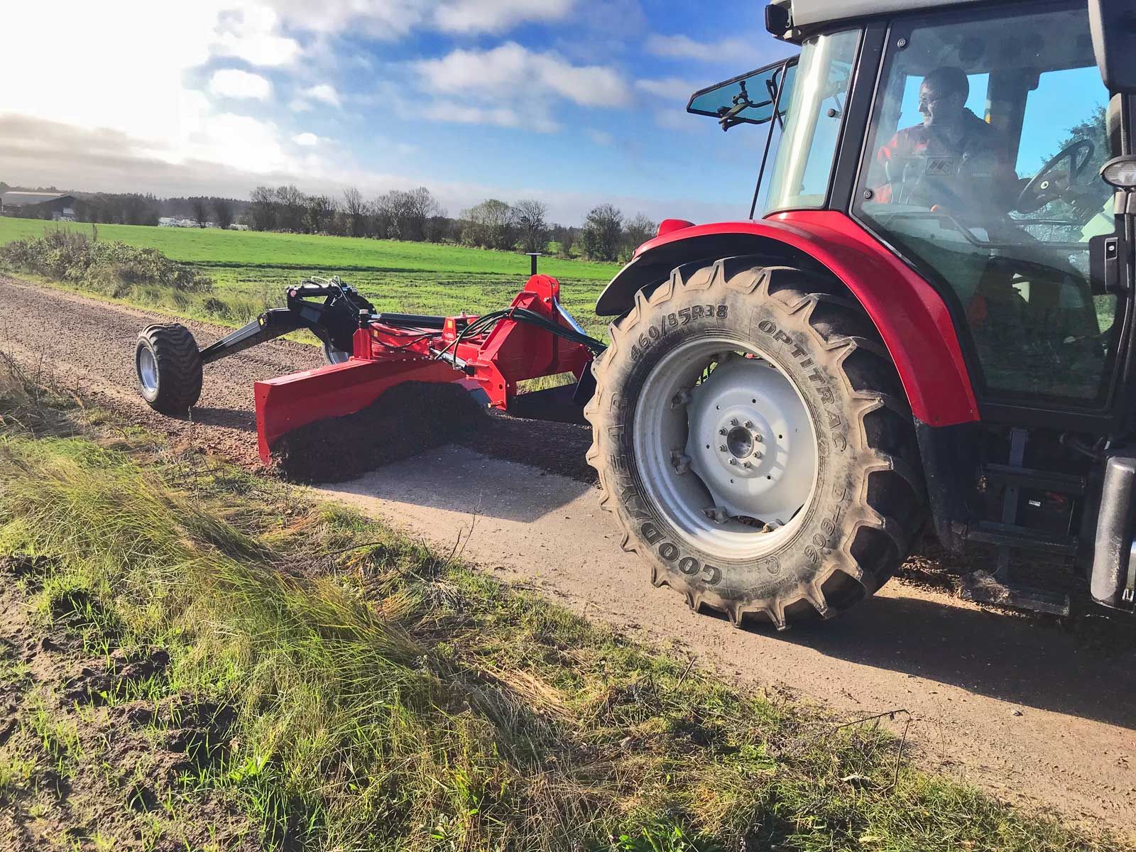 Ein roter Traktor fährt einen Feldweg entlang.