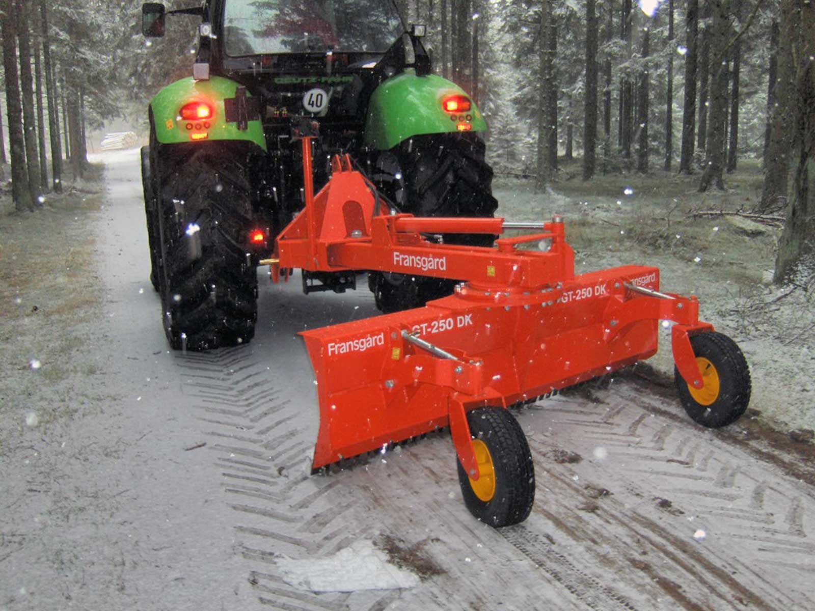 Ein grün-orangefarbener Traktor fährt eine verschneite Straße entlang