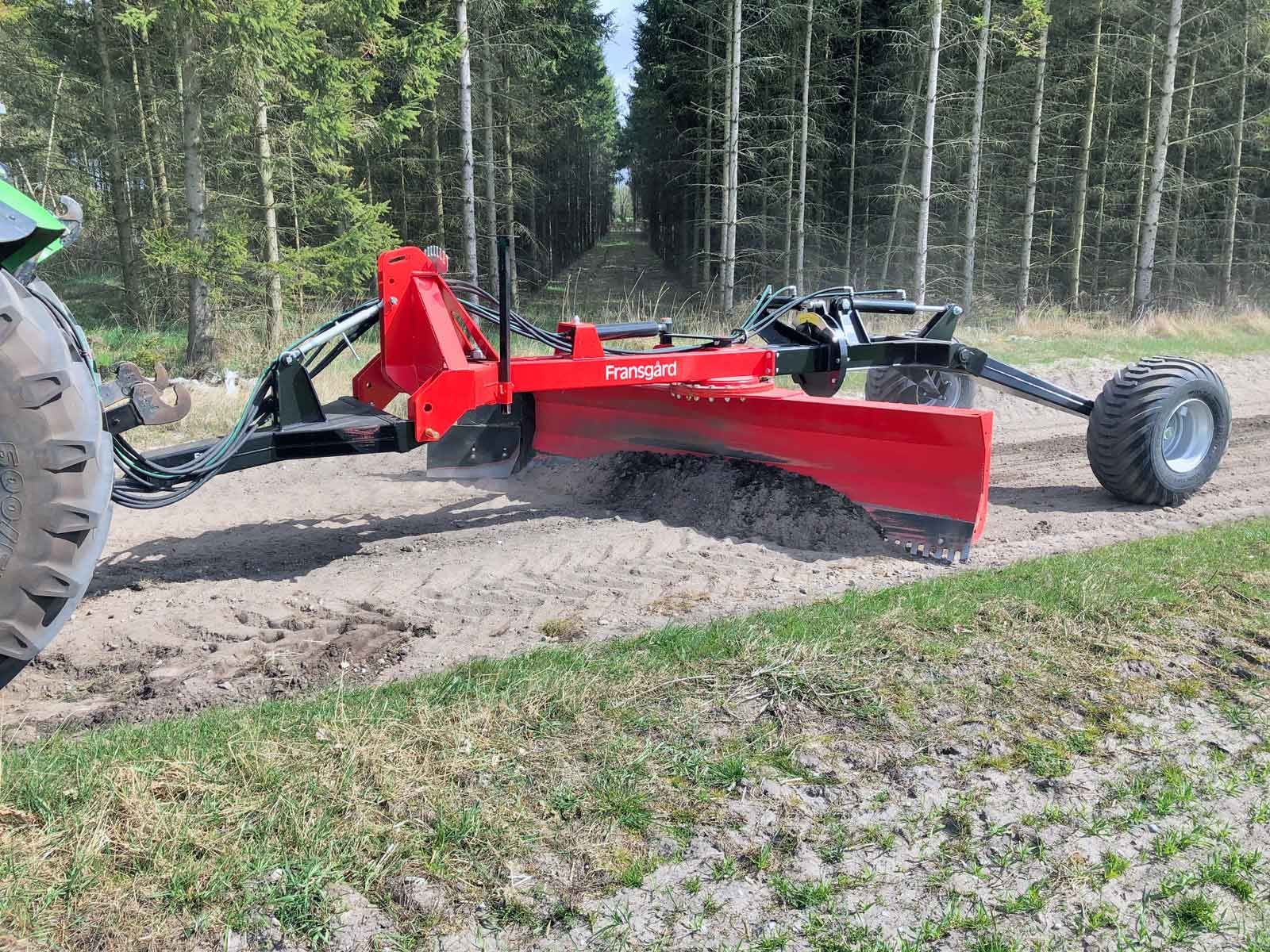 Ein rot-schwarzer Traktor räumt einen Feldweg.