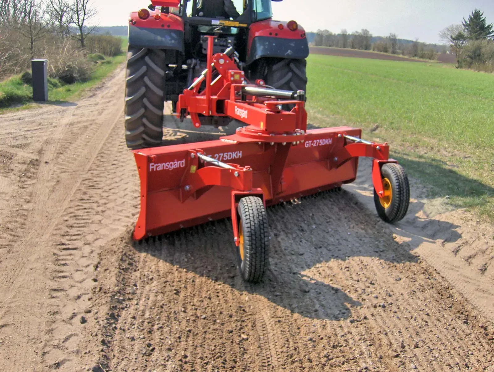 Ein roter Traktor fährt eine unbefestigte Straße entlang
