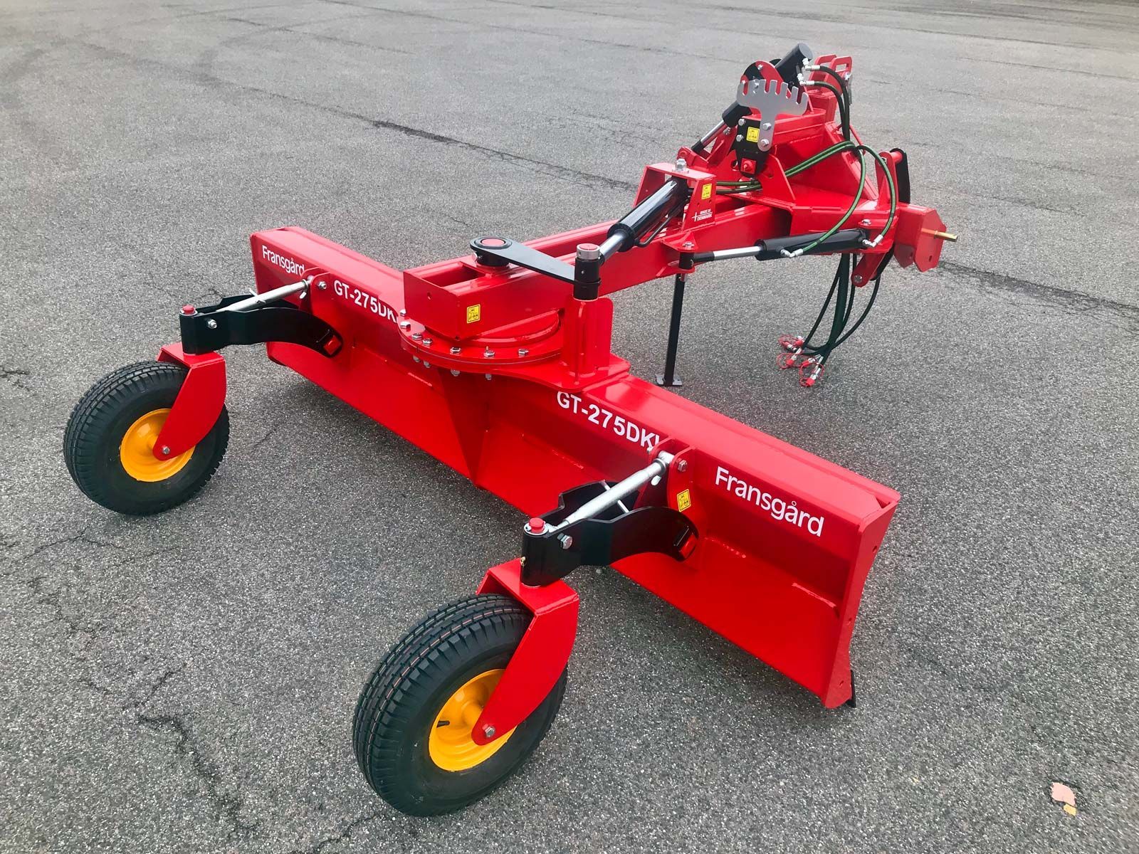 Ein roter Traktor mit gelben Rädern steht am Straßenrand.