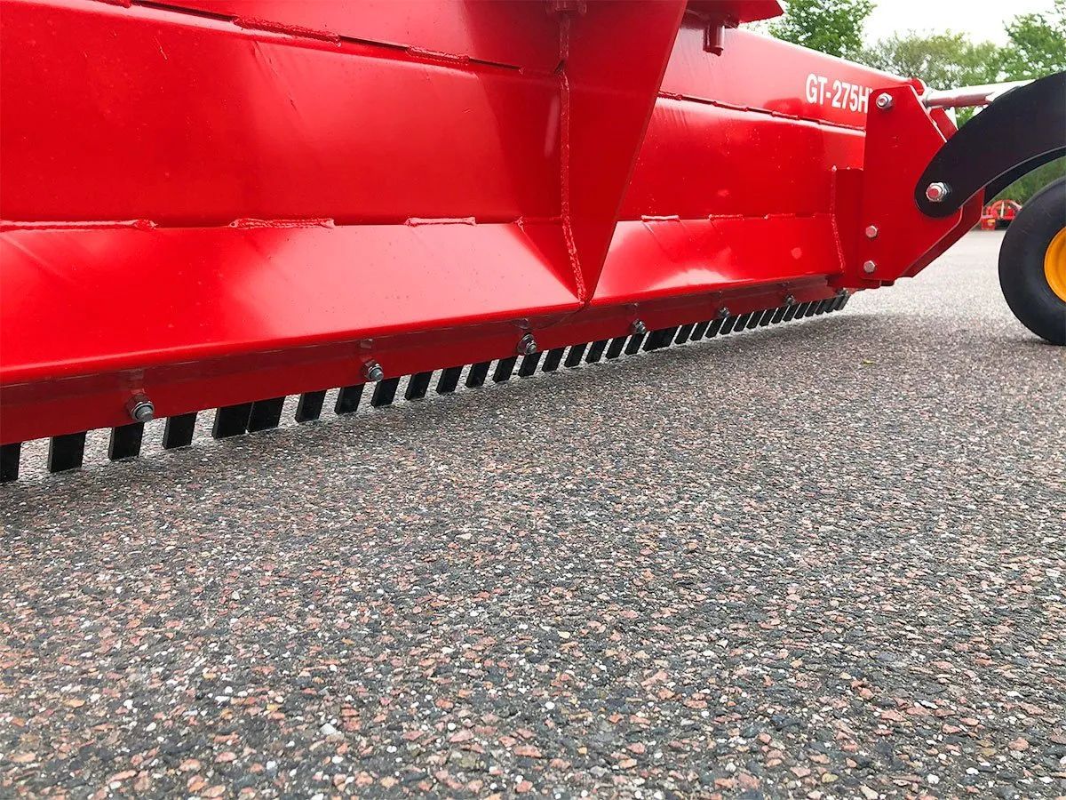 Ein roter Traktor parkt auf einer Schotterstraße.
