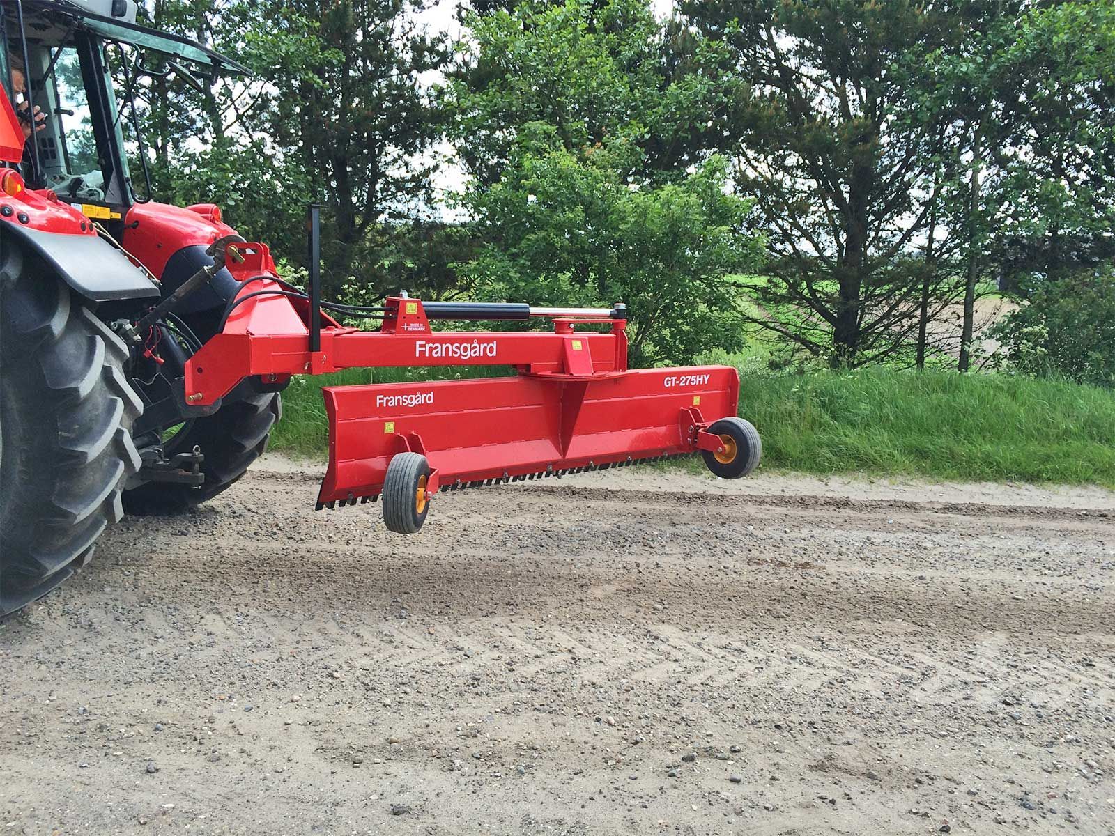 Ein roter Traktor fährt einen Feldweg entlang.