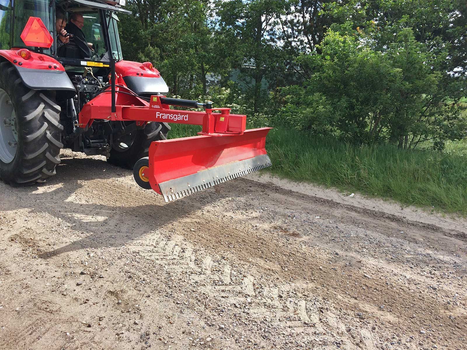 Ein roter Traktor fährt einen Feldweg entlang.