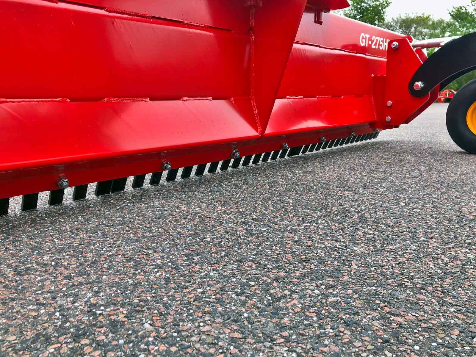 Ein roter Traktor parkt auf einer Schotterstraße.