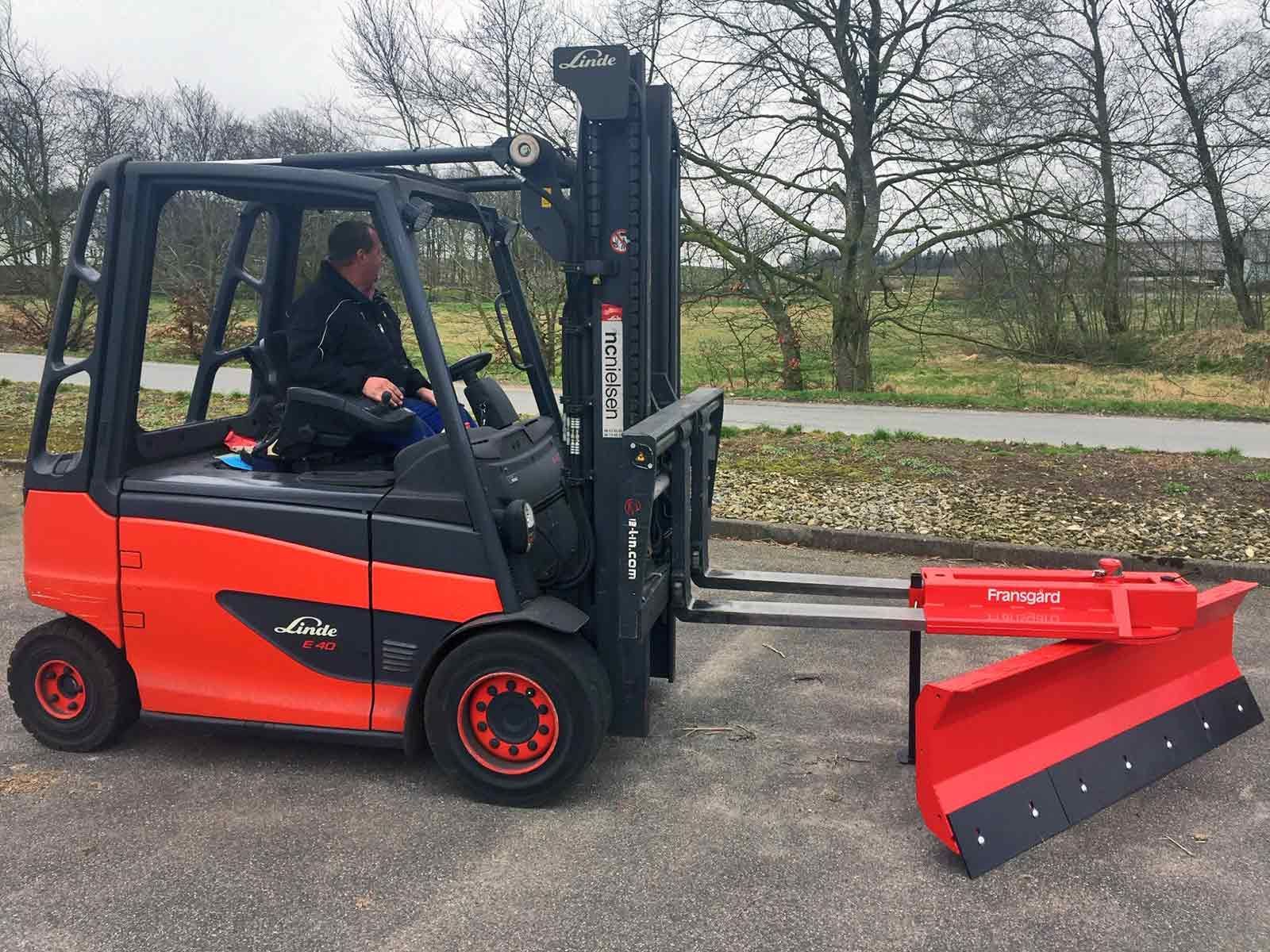 Ein Mann fährt einen Gabelstapler, an dem ein Pflug befestigt ist.