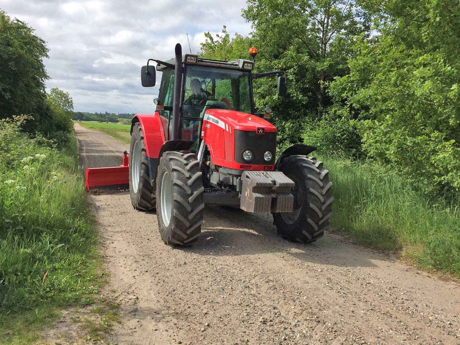 Ein roter Traktor fährt einen Feldweg entlang.