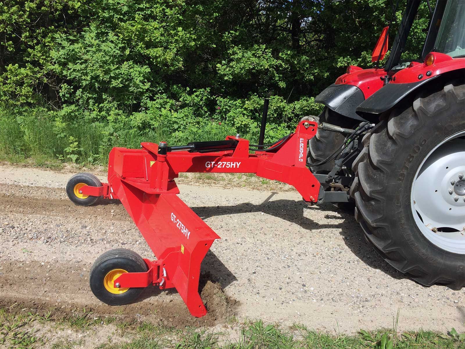 Ein roter Traktor fährt einen Feldweg entlang.