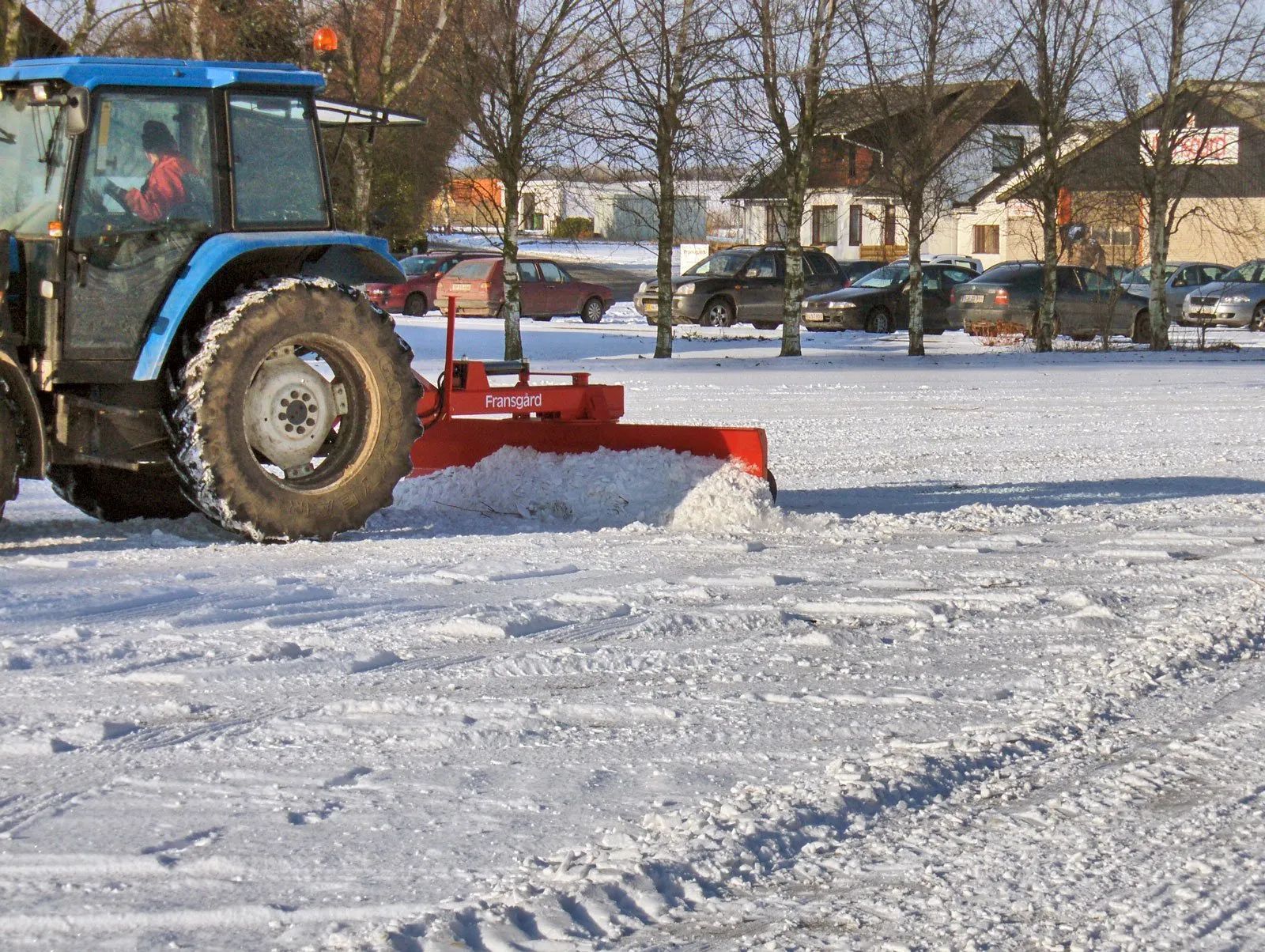 Ein blauer Traktor räumt Schnee auf einem Parkplatz