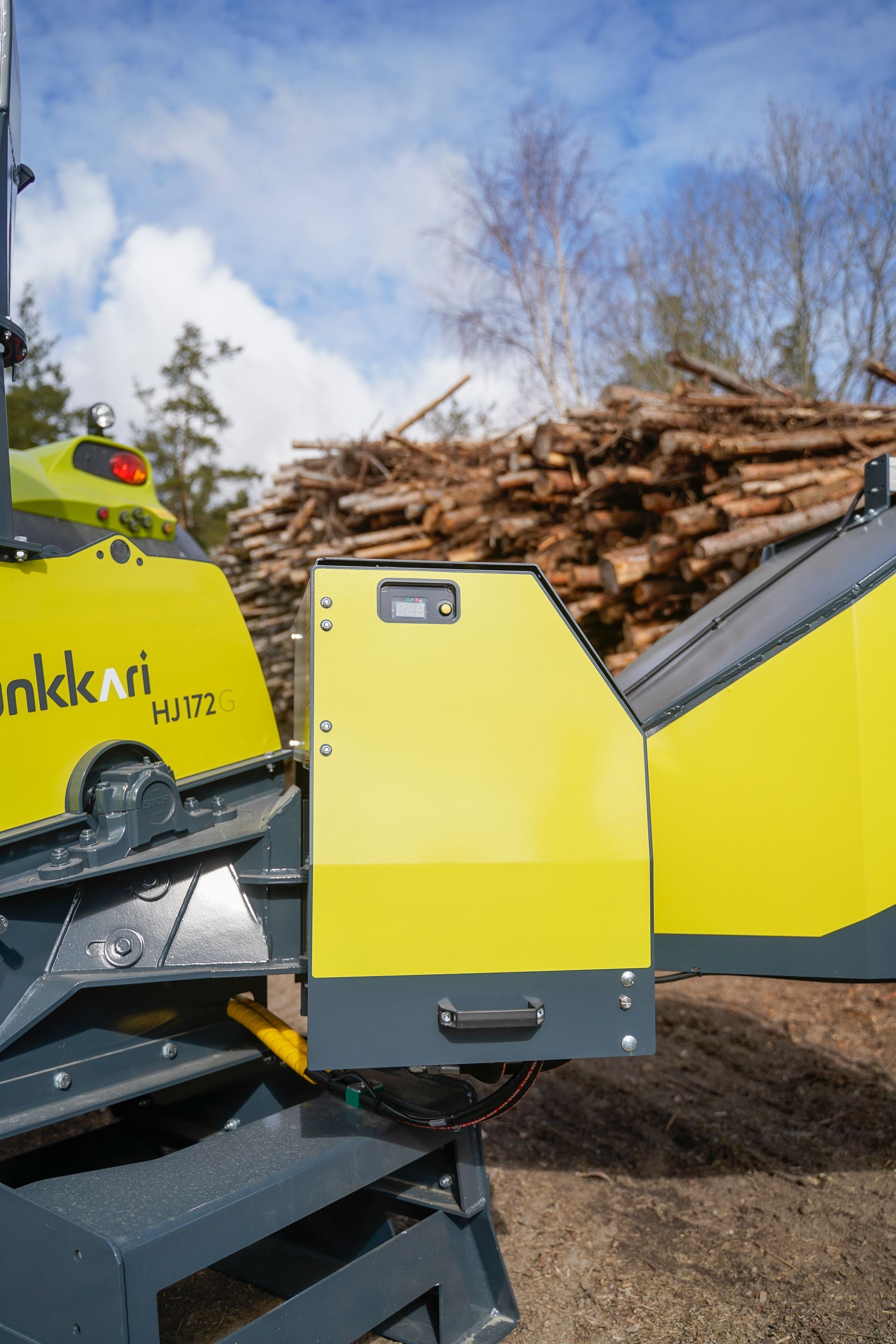 Eine gelb-graue Maschine steht vor einem Stapel Holzstämme.