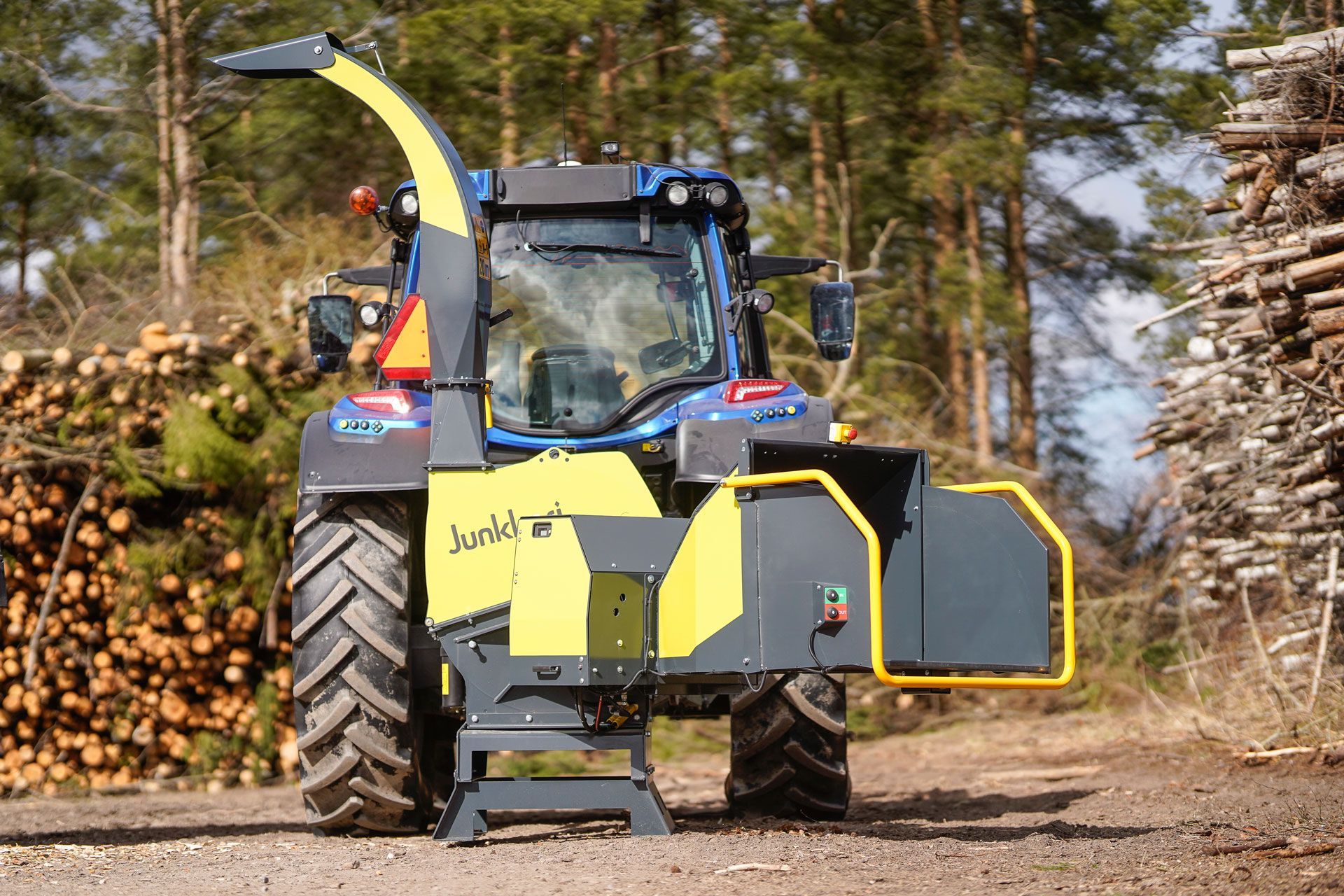 Vor einem Stapel Holzstämme hackt ein Traktor Holz.