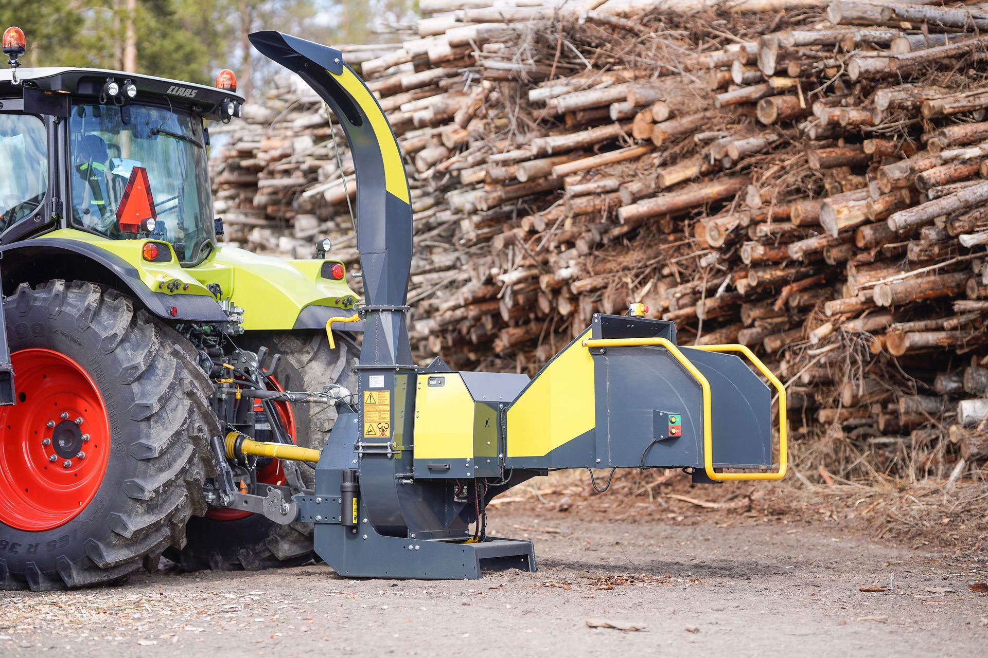 Vor einem Stapel Baumstämme steht ein Traktor.