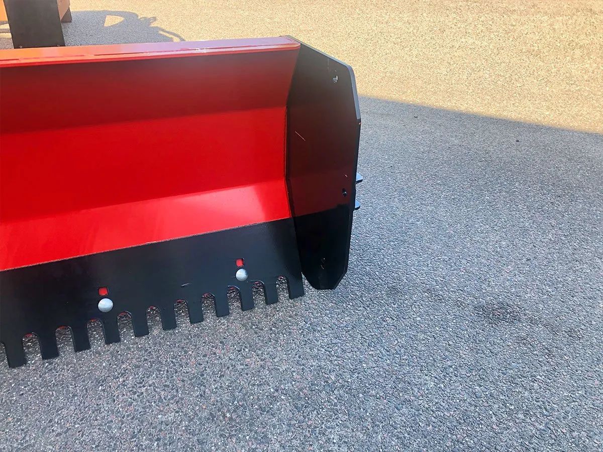 Auf einer Schotterstraße steht ein rot-schwarzer Schneepflug.