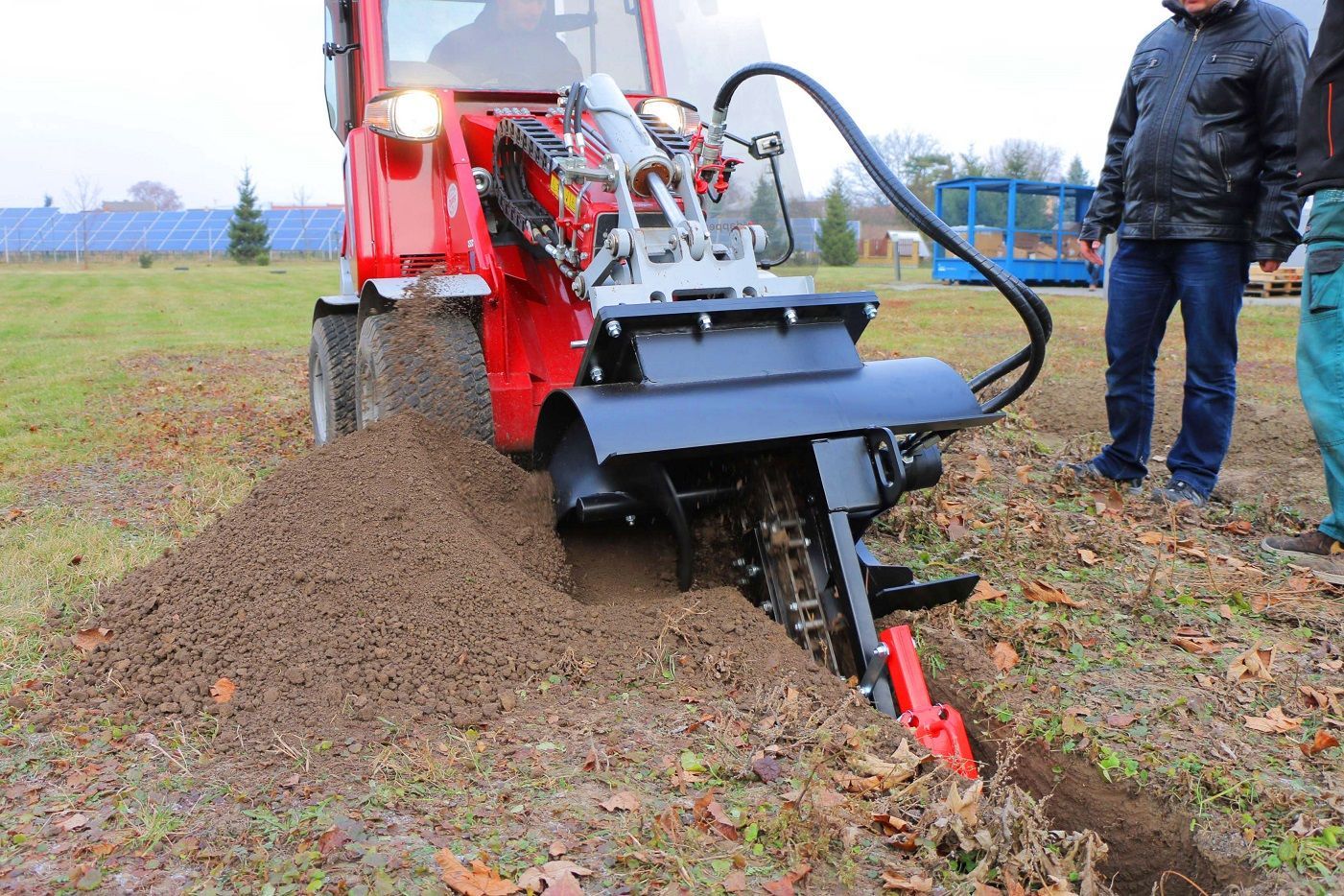 Ein Mann steht neben einem Traktor, der ein Loch in den Boden gräbt.