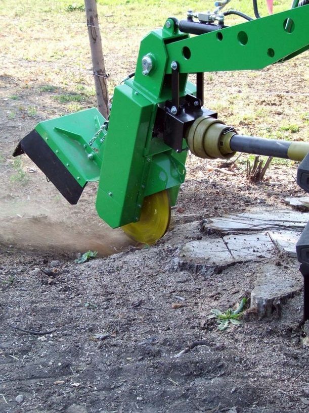 Eine grüne Maschine schneidet einen Baumstumpf in den Dreck