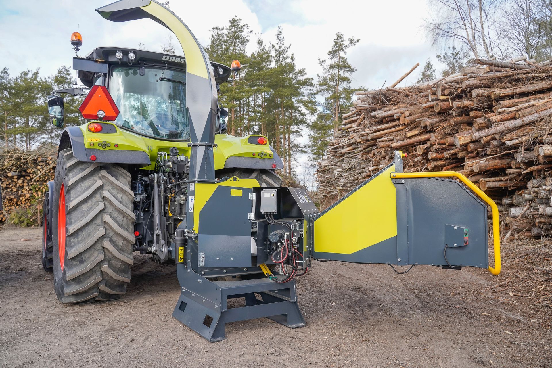 Vor einem Stapel Baumstämme steht ein Traktor.