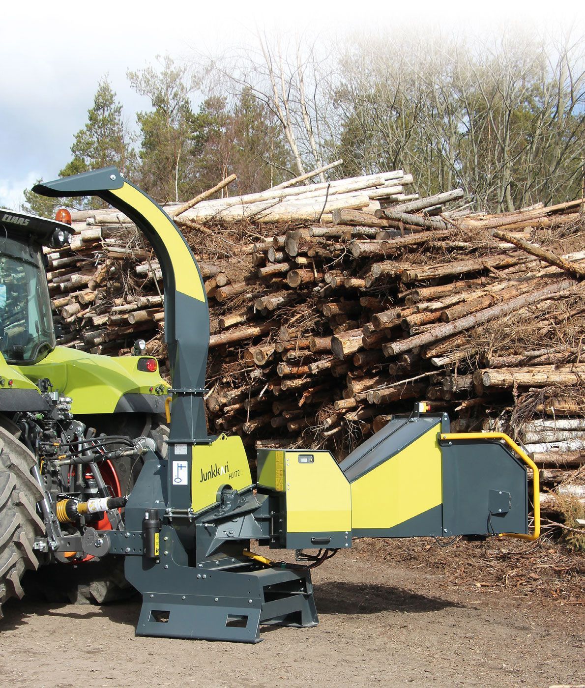 Ein gelb-schwarzer Traktor steht vor einem Stapel Baumstämme.