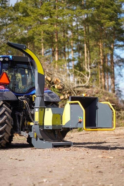 Ein Traktor fährt auf einer unbefestigten Straße neben einem Baumhäcksler her.